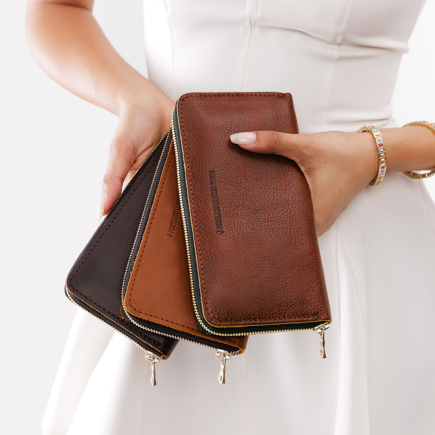 All Variants |  | Model holding three large accordion leather wallets with zippers