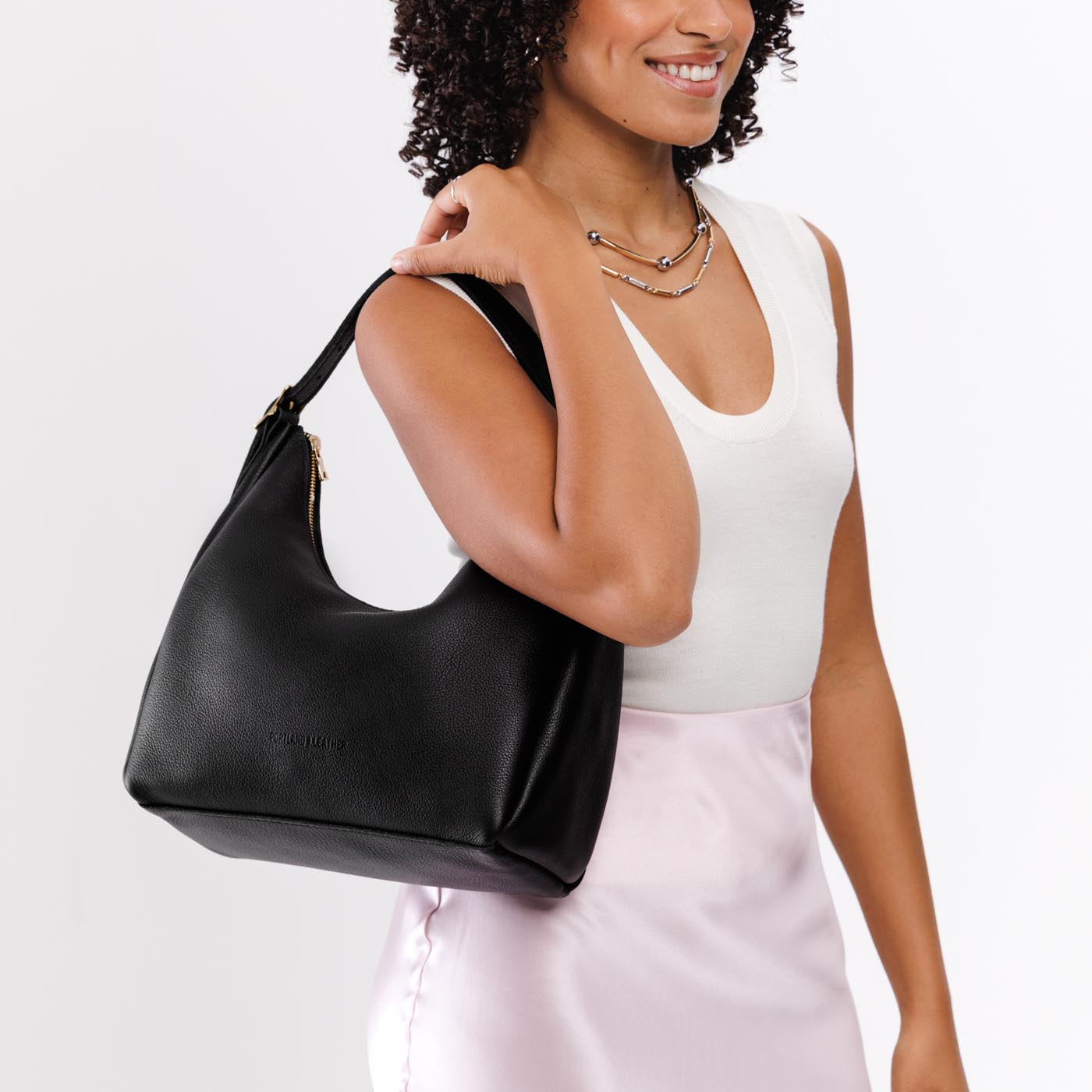 Pebbled--black*Medium | Model holding u-shaped, flat-bottomed leather shoulder bag with adjustable strap
