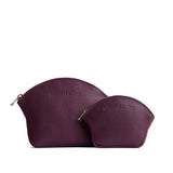 Plum | Comparison shot of small and large seashell shaped leather makeup bags with curved top zipper and flat bottom