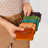 All Variants | Model holding five different colored wallets with snap closures