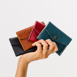 All Variants | Model hand holding four small leather envelope wallets with snap closures