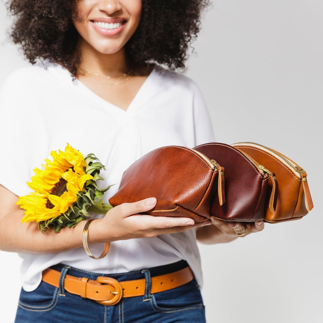 All Variants | Model holding three spacious leather makeup bags with curved seams and top zipper