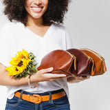 All Variants | Model holding three spacious leather makeup bags with curved seams and top zipper